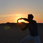 Person creating the illusion of holding the sun between their hands at sunset in a desert.